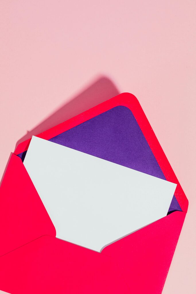 Open red envelope with purple liner and white card on a pink surface. Modern minimalist style.